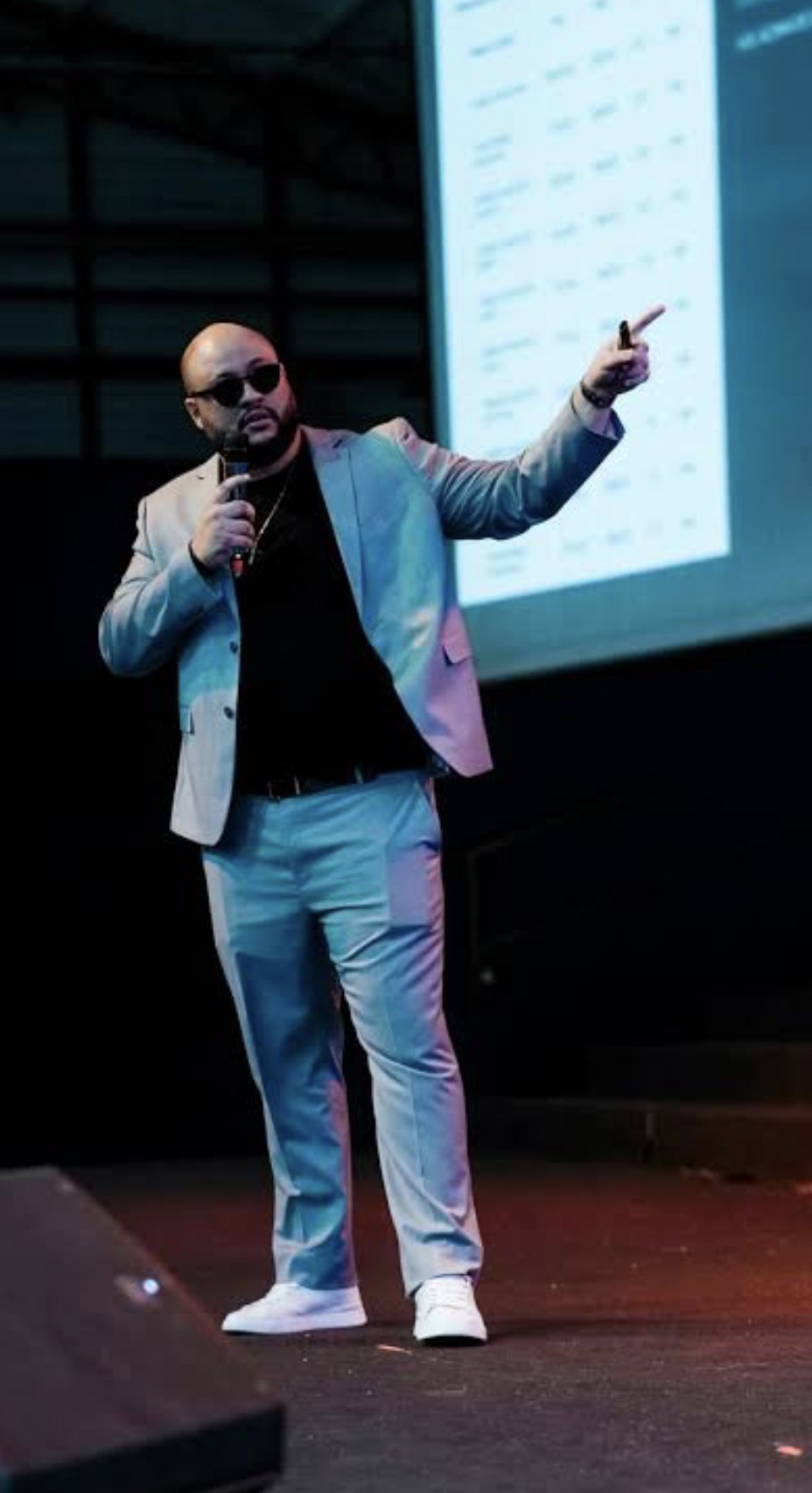 Em pé no palco, de microfone na mão, durante uma palestra — Guga Stefano.